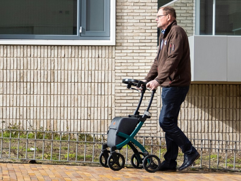 oudere man met rollator loopt op de stoep